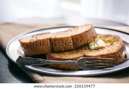 Two pieces of French toast with butter on a silver plate.