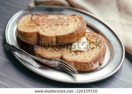 Two pieces of French toast with butter on a silver plate.
