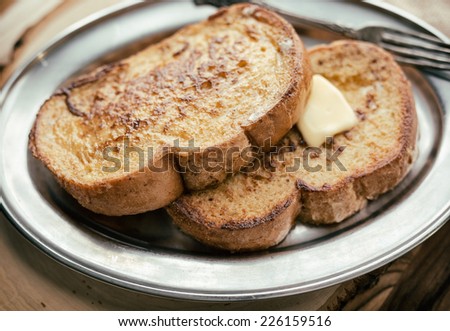 Two pieces of French toast with butter on a silver plate and wooden board.