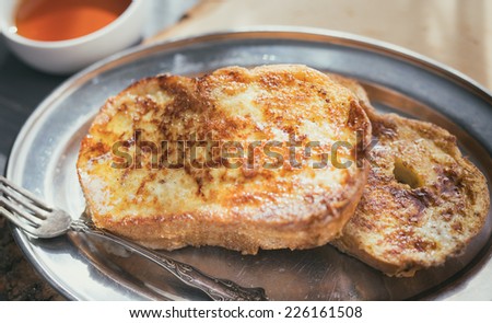 Two pieces of French toast with butter and a small ramekin of maple syrup on a silver plate.
