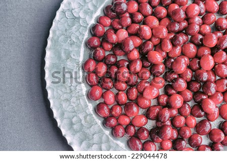 A bunch of raw cranberries on a hammered silver platter against a gray background.  Analog filter.