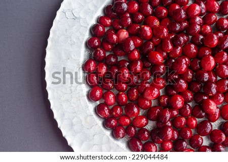 A bunch of raw cranberries on a hammered silver platter against a gray background.