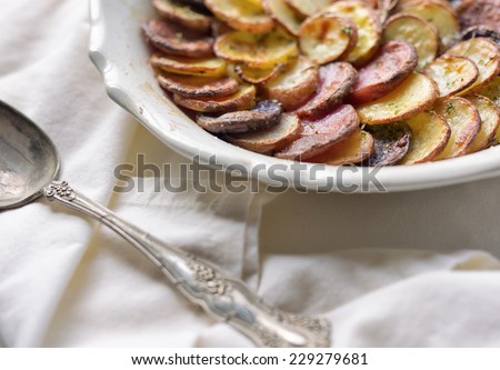 Sliced and roasted potatoes with rosemary and a silver serving spoon in a shallow baking dish.