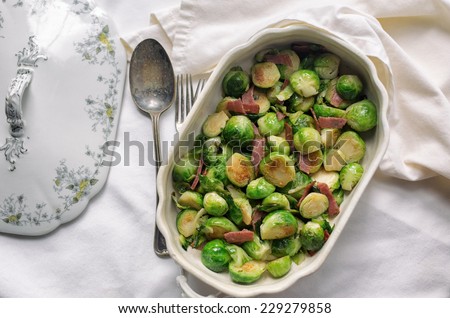 Fresh sauteed Brussels sprouts with ham and silver spoon in an ornate serving dish.