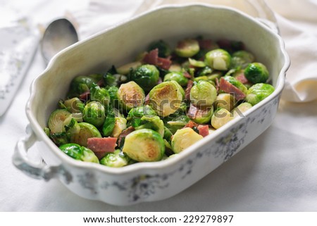 Fresh sauteed Brussels sprouts with ham and silver spoon in an ornate serving dish.