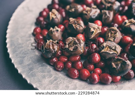 Raw cranberries and roasted chestnuts on a hammered silver platter and gray tablecloth. Analog and vintage filters applied.