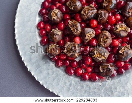 Raw cranberries and roasted chestnuts on a hammered silver platter and gray tablecloth.