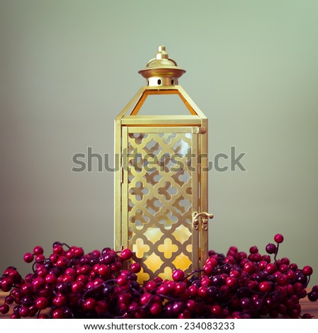 Gold lantern against light green background with a wreath made of holly berries.  Analog filter.
