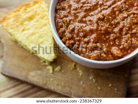 Bowl of chili with a piece of cornbread on a wooden background.