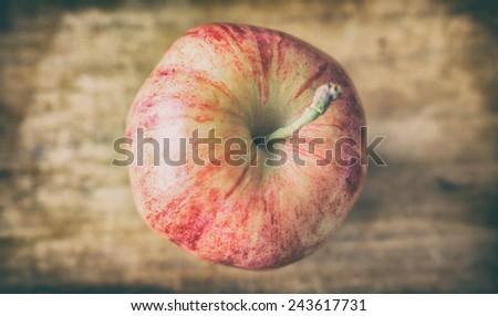 View from above of one gala apple with stem on a wood cutting board.