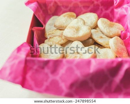 Red gift box with hot pink tissue paper filled with heart shaped pastries for Valentine\'s Day.  Vintage filter applied.