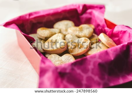 Red gift box with hot pink tissue paper filled with heart shaped pastries for Valentine\'s Day.