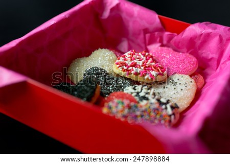Gift box lined with pink tissue paper filled with various Valentine\'s day cookies.  Black background.