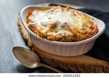 Individual serving of baked ziti covered in melted cheese with napkin and spoon.