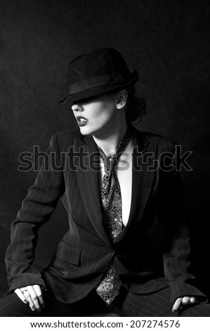 Woman dressed in man\'s suit and tie with trilby hat covering eyes