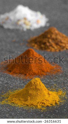 Four colorful piles of ground spices on grey background