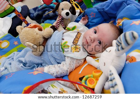 Beautiful baby lying in bed surrounded by many toys
