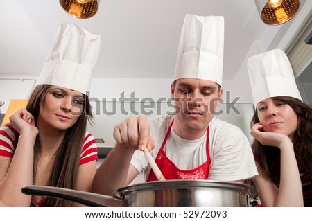Young man with chef\'s hat stirring food while two girls are watching