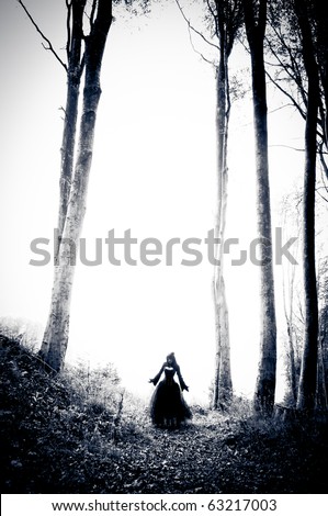 Scary woman from nightmares in black dress with trees around her