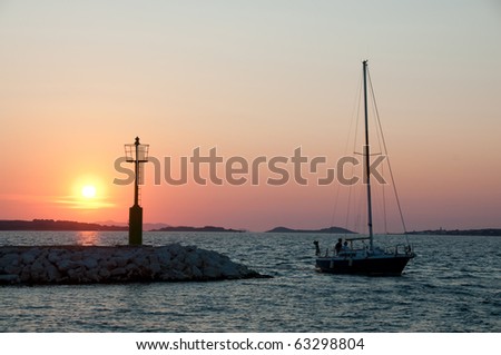 Sailing boat passing light beacon in sunset