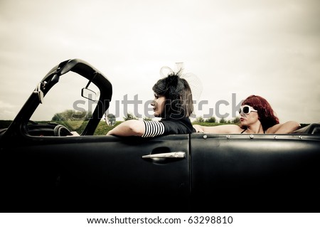  photo Side view of two attractive girls driving around in vintage car