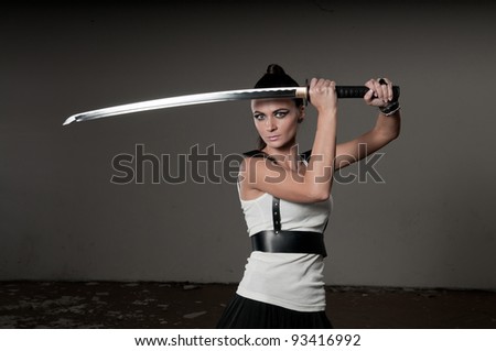 Beautiful woman holding a long shining steel ceremonial sword above her head with copyspace.