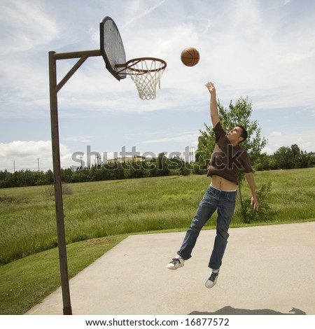 Young man jumping up to rebound a goal on a bright sunny day on an outdoor basketball court.