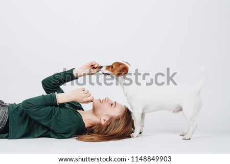 Young woman plays with her jack russell terrier dog isolated on white background. Girl lies down and looks up on her dog. Owner and dog have fun. Studio portrait.