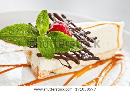 Cheesecake with raspberry, chocolate, mint twig, powdered sugar, and caramel