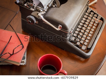 black retro typewriter sitting on wooden coffee table and cup of coffee, old worn books and stylish glasses are good for authors, writers, editors or journalists