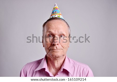 Mature man with funny face and happy birthday paper hat on grey background