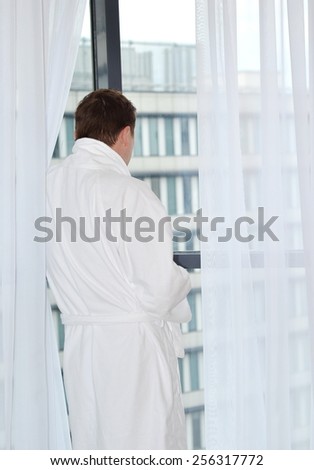 Back view of Young man in bathrobe looking at window