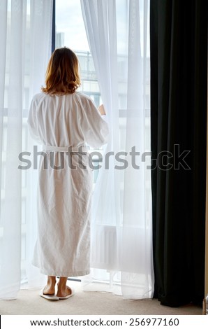 Back view of slim woman in a white bathrobe in front of a window