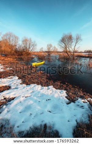 Early spring landscape with a wooden boat on a flooded river and thawed ice.