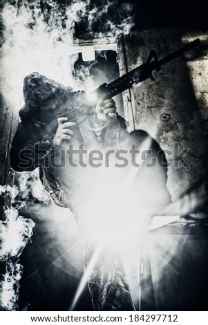 Soldier with rifle aiming against strong light covered in smoke