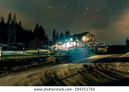 Mountain cottage under the stars at night with cloudy sky
