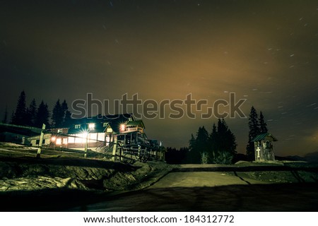 Mountain cottage under the night sky with star trails