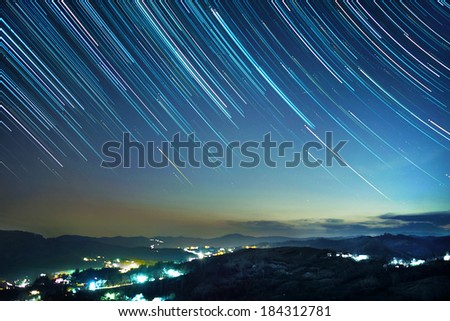 Mountain resort at night under cloudy sky with star trails