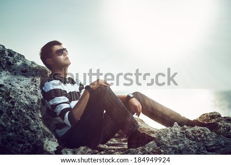 Young man standing on a cliff at sunset looking at the sky