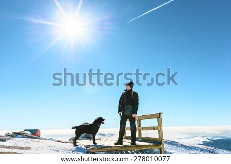 Man with dog resting and admiring the beauty of snowy mountains landscape