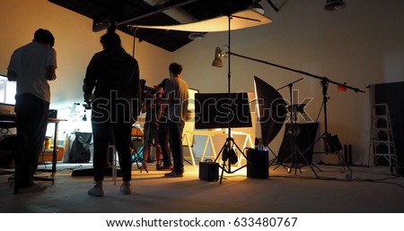 Behind the shooting production crew team and silhouette of camera and equipment in studio.
