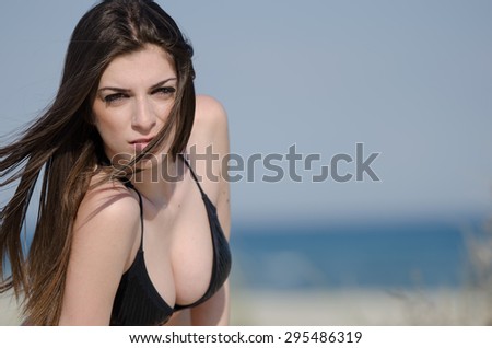 Good looking lady with long hair, lying on sand and the wind blowing her hair covering the face, her breast looks great