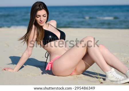 Attractive woman, model from Greece lying at the sand with bikini , the wind blowing her hairs, at the background sea and sky