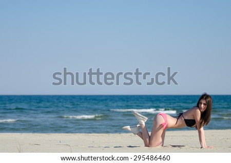 Attractive woman kneels at the sand with bikini and shoes, at the background sea and sky. The photo is full length body with copy space