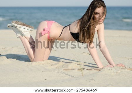 Attractive woman kneels at the sand with bikini and shoes, at the background sea and sky