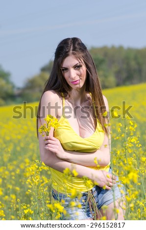 Yellow blooming field, cute fit young lady in yellow shirt. She is hugging herself and holds a bouquet of yellow flowers