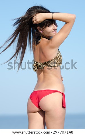 Back view of lady wearing red and animal print striped bikini, she play with hairs and filling the wind. Sea and sky as background