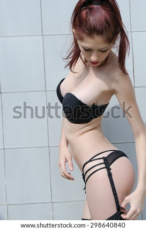 Sexy lingerie woman standing against wall tile in the bathroom holding and fixing the suspender belt