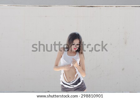 Slim female standing behind of a cement window wearing torn shirt, straight hair and bolt red lips