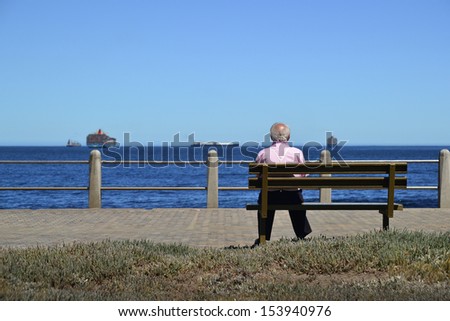 Old man sitting on the bench by the see and gazing on ships